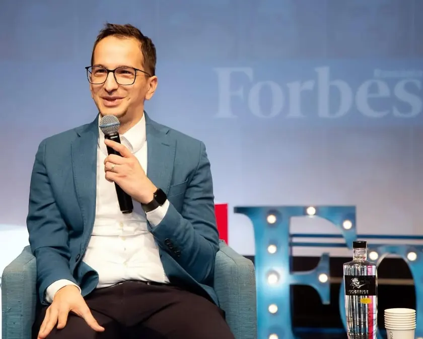 Laur Neagu of Unicorn IT Services speaking into a microphone on stage in front of a Forbes Romania backdrop