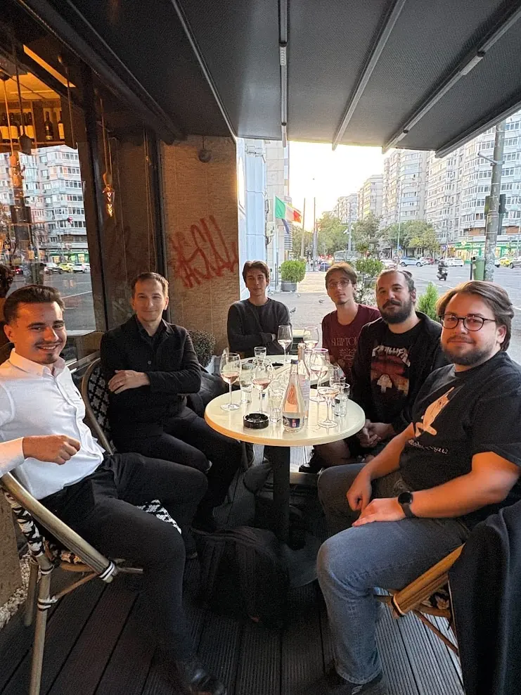 Seven members of the Unicorn IT Services team sitting around a café table on a Bucharest street